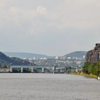 Pohled na Ústí nad Labem přes řeku, s plavebním zdymadlem, skalním svahem a městem v údolí pod zataženou oblohou