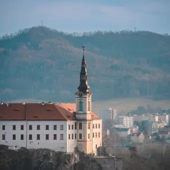Pohled na kostelní věž v Děčíně nad městskou zástavbou, s kopci v pozadí