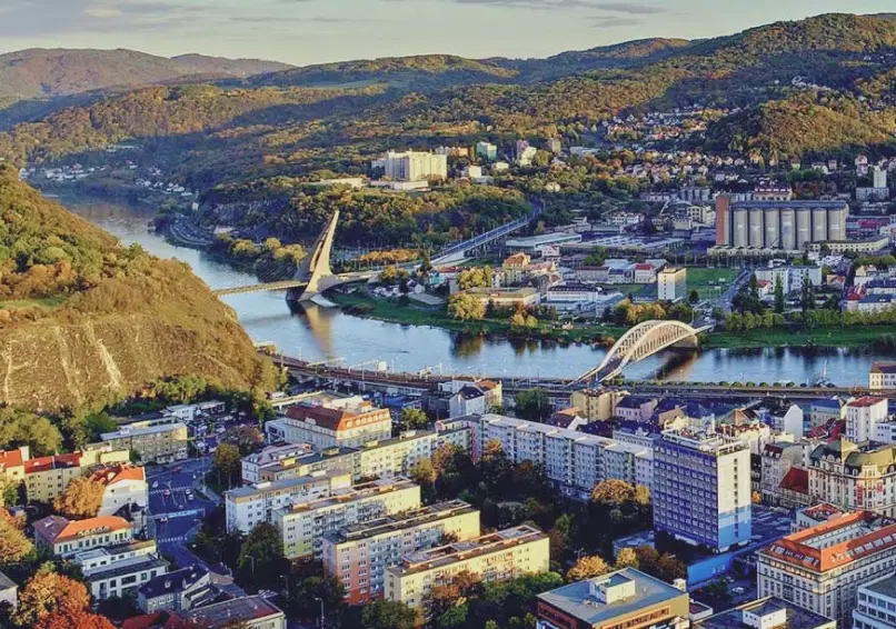 Pohled na Ústí nad Labem přes řeku, s plavebním zdymadlem, skalním svahem a městem v údolí pod zataženou oblohou