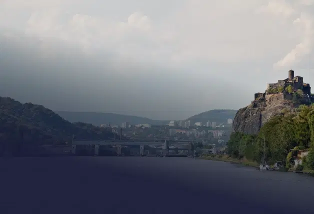 Pohled na Ústí nad Labem přes řeku, s plavebním zdymadlem, skalním svahem a městem v údolí pod zataženou oblohou