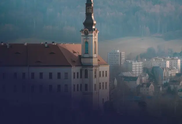 Pohled na kostelní věž v Děčíně nad městskou zástavbou, s kopci v pozadí