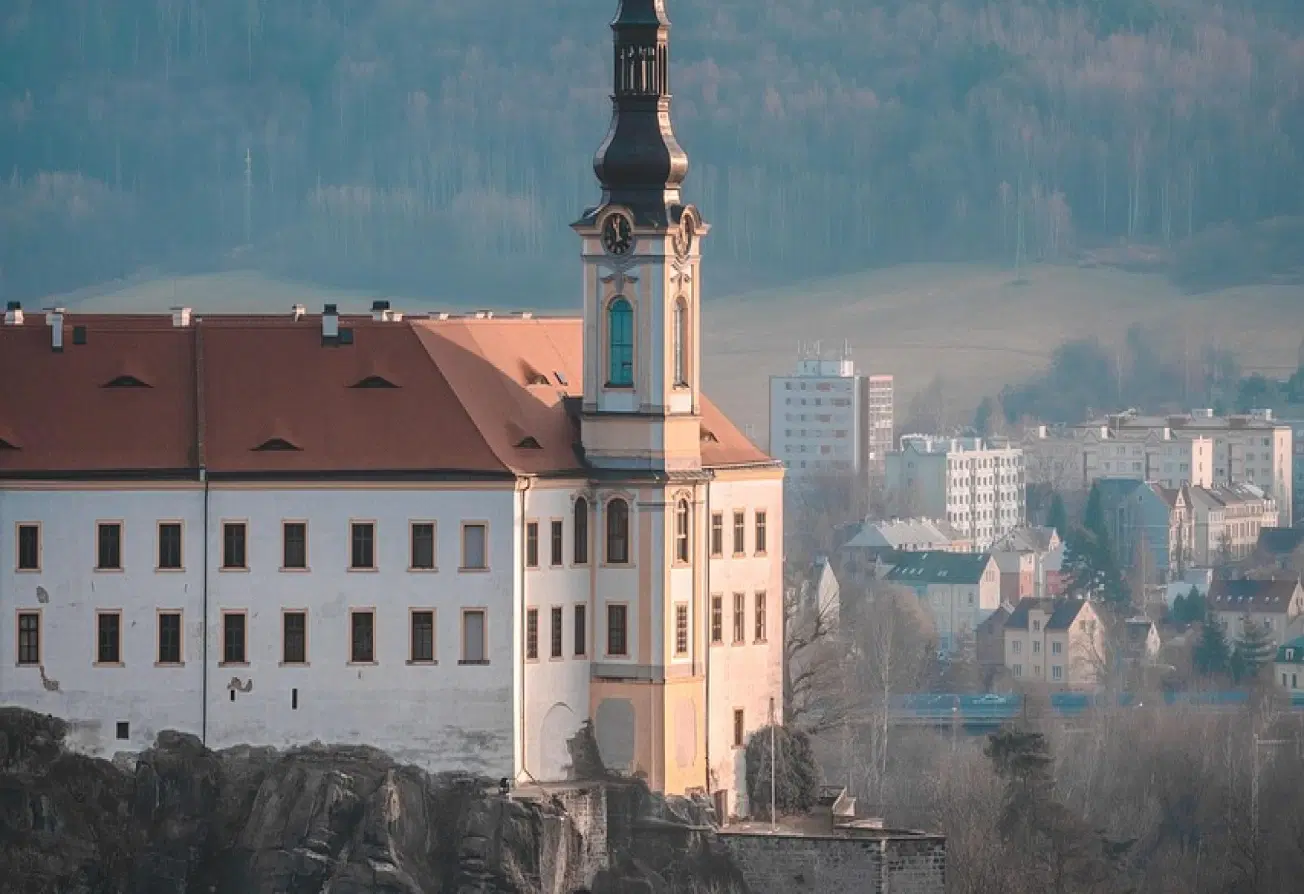 Pohled na kostelní věž v Děčíně nad městskou zástavbou, s kopci v pozadí