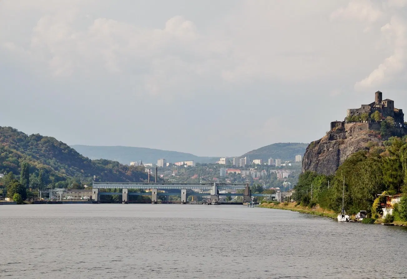 Pohled na Ústí nad Labem přes řeku, s plavebním zdymadlem, skalním svahem a městem v údolí pod zataženou oblohou