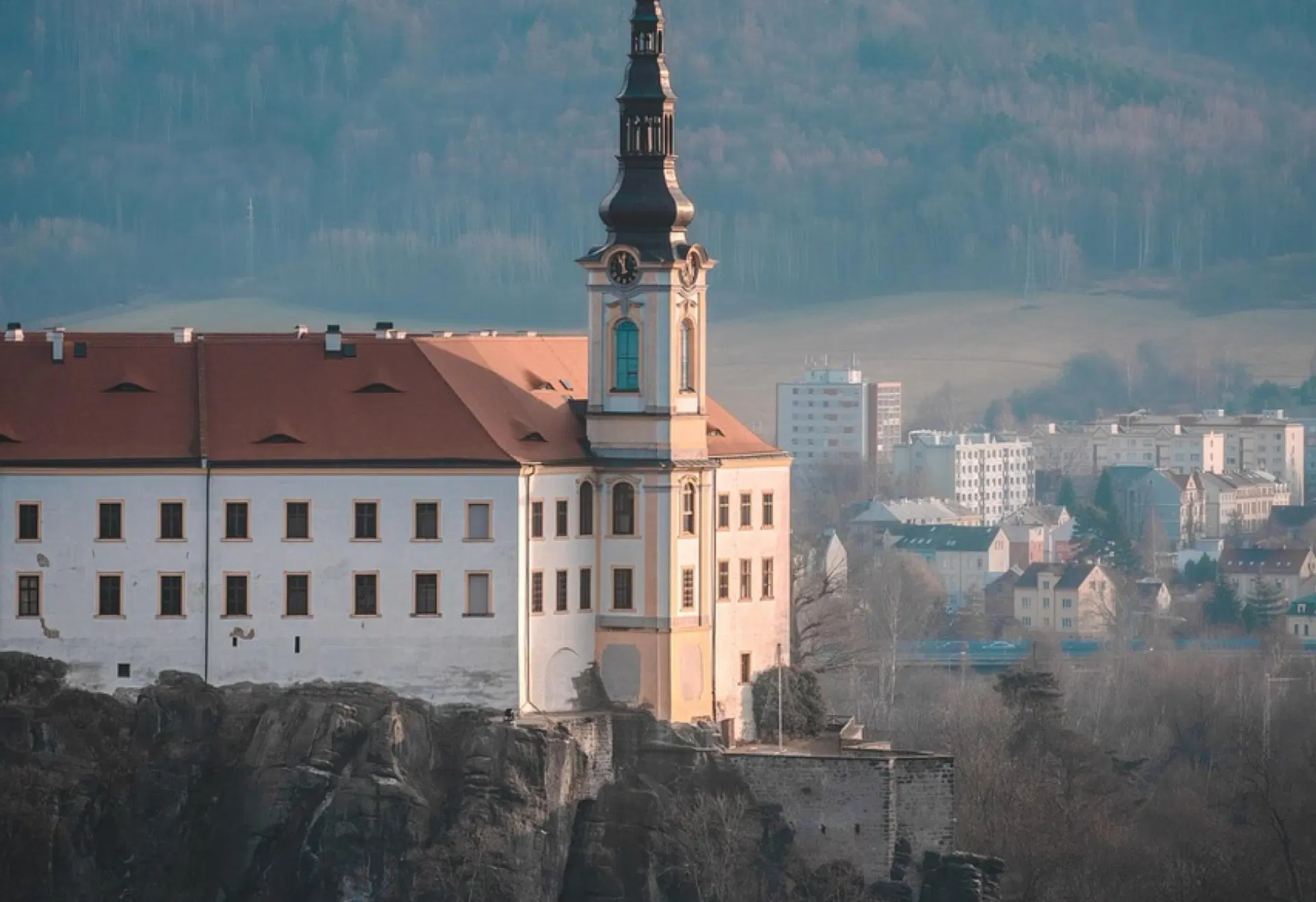 Pohled na kostelní věž v Děčíně nad městskou zástavbou, s kopci v pozadí
