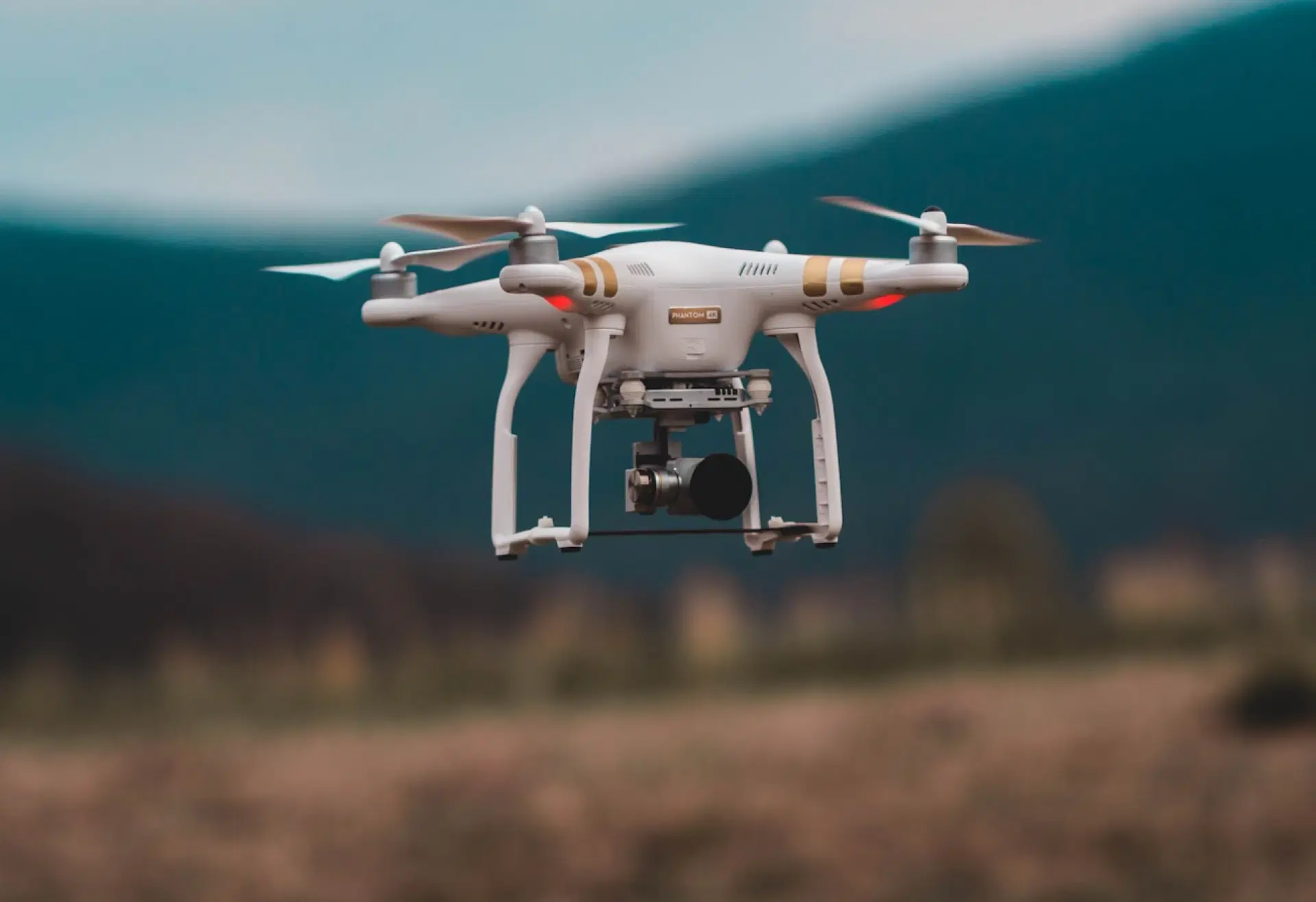 Bílý dron s kamerou se vznáší před rozostřeným pozadím