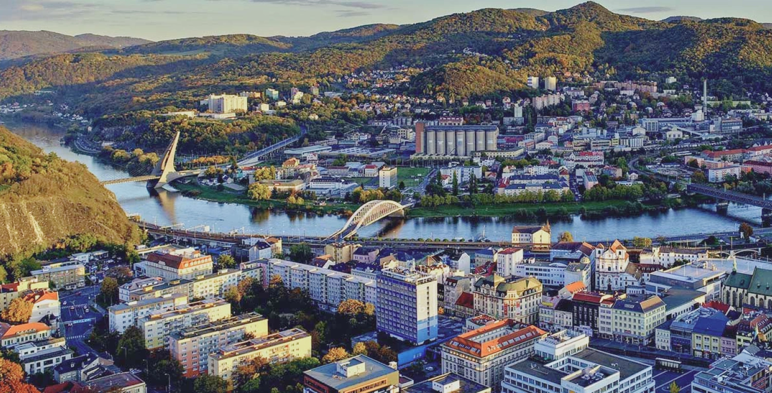 Pohled na Ústí nad Labem přes řeku, s plavebním zdymadlem, skalním svahem a městem v údolí pod zataženou oblohou