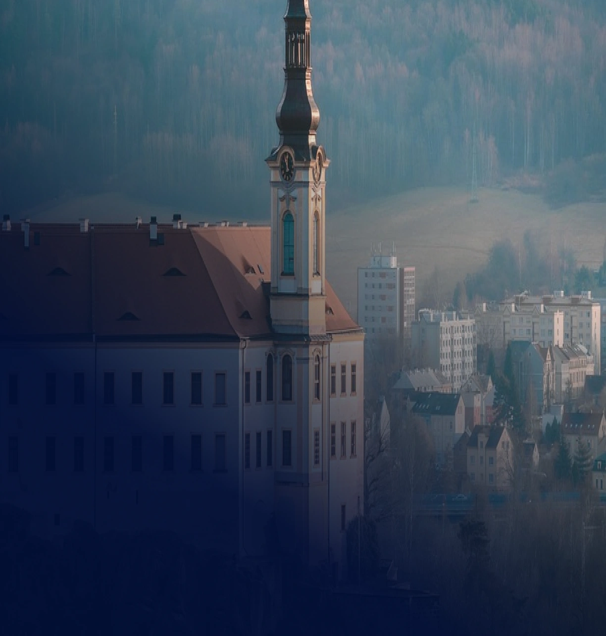 Pohled na kostelní věž v Děčíně nad městskou zástavbou, s kopci v pozadí