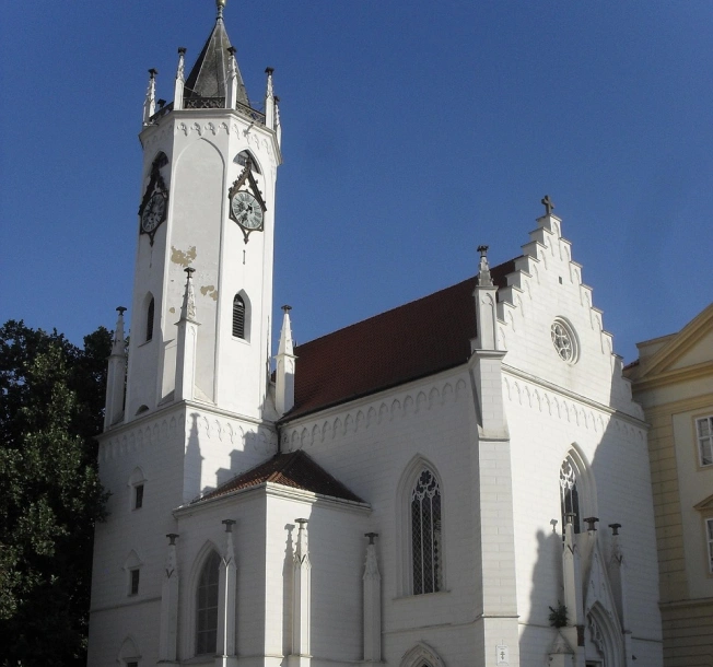 Bílý kostel s vysokou věží a hodinami v Teplicích, focený zespodu proti modré obloze