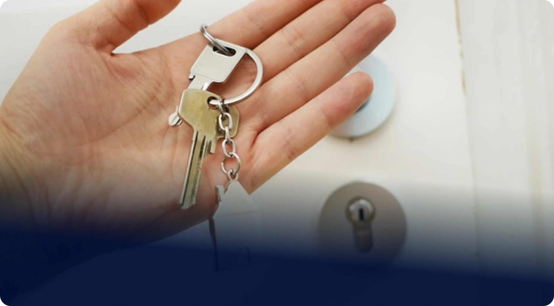 Otevřená dlaň drží svazek klíčů od domu před dveřním zámkem