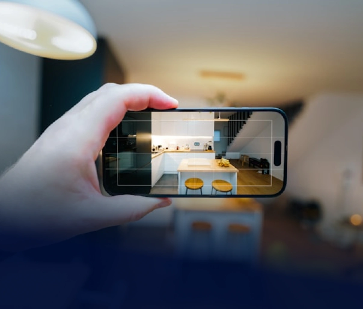 Ruka drží telefon, který fotografuje moderní kuchyň s ostrůvkem